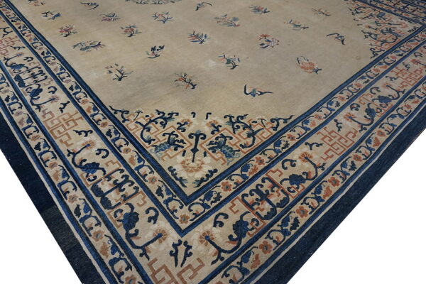 Low-pile tan rug featuring a scattered floral pattern and contrasting wide dark blue patterned border.
