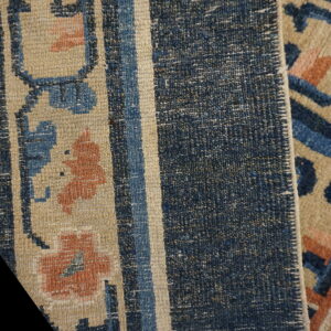 Detailed view of a beige rug with blue and rust geometric floral patterns and a densely woven blue striped edge.