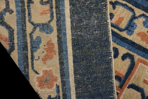 Detailed view of a beige rug with blue and rust geometric floral patterns and a densely woven blue striped edge.