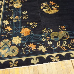 Dark blue rug with floral and medallion patterns in gold, orange, and blue on distressed wood floor.