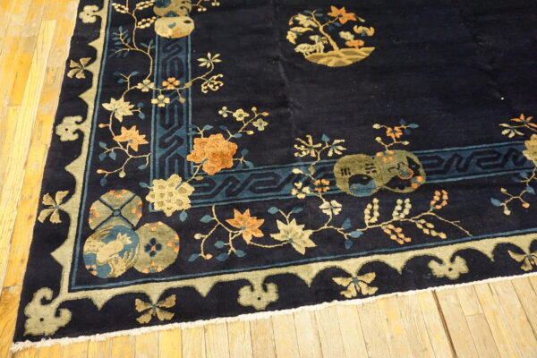 Dark blue rug with floral and medallion patterns in gold, orange, and blue on distressed wood floor.
