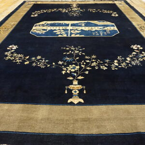 Large navy blue rug with a gold border features floral vines and a blue landscape cartouche on wood flooring.