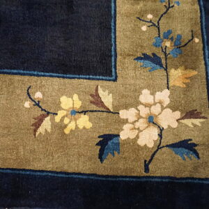 Navy blue rug border with olive floral motif of cream, yellow, and blue flowers on wood flooring.