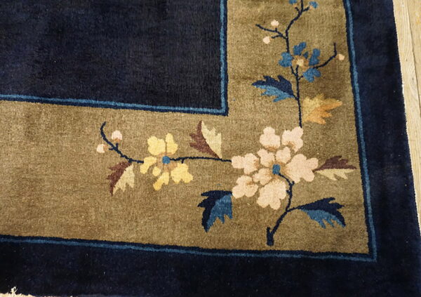 Navy blue rug border with olive floral motif of cream, yellow, and blue flowers on wood flooring.