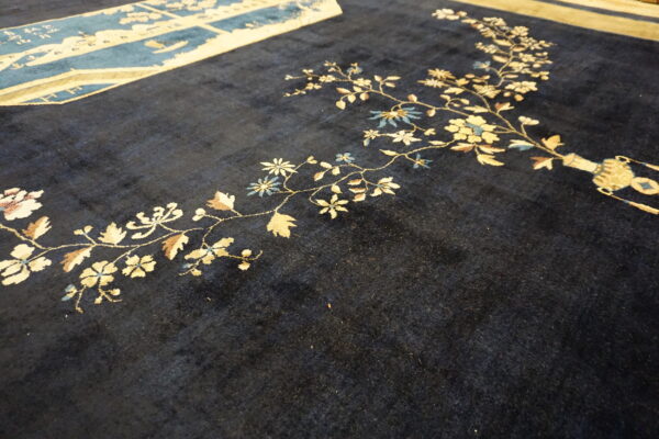 Dark blue rug field showing cream and pale blue floral vines next to a patterned blue border section.
