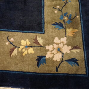 Navy and olive high-pile rug corner featuring a multicolored floral pattern on light wooden flooring.