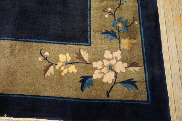 Navy and olive high-pile rug corner featuring a multicolored floral pattern on light wooden flooring.