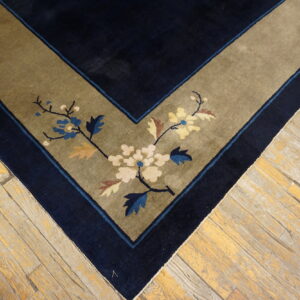 Navy rug corner with an olive border displays cream and blue blossoms on light, distressed wood floors.