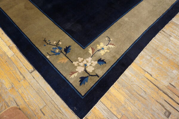 Navy rug corner with an olive border displays cream and blue blossoms on light, distressed wood floors.