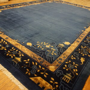 Deep blue rug featuring a wide scenic border with gold floral motifs, birds, and pagodas on wood plank flooring.
