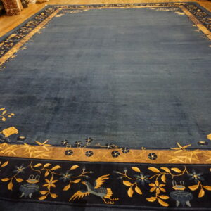 Deep blue rug with complex gold and indigo pictorial borders displayed on a wood floor.