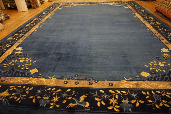 Deep blue rug with complex gold and indigo pictorial borders displayed on a wood floor.
