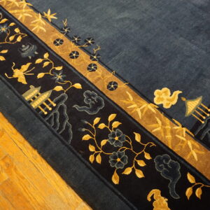 A detailed navy rug with gold borders, vines, and temple motifs is placed on wood plank flooring.