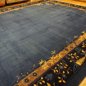 A deep blue rug featuring complex yellow and navy patterned borders lies on a light wooden floor.
