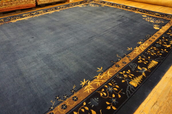 A deep blue rug featuring complex yellow and navy patterned borders lies on a light wooden floor.