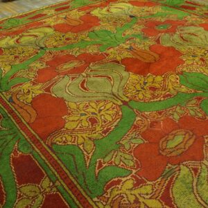 Stylized floral rug featuring large leaves and blossoms in red, green, and gold on a plank floor.