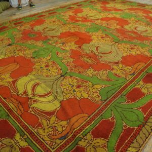 Vibrant orange rug with large green and yellow botanical patterns on light wood planks.