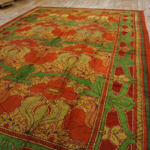 A thick-pile rug with large red flowers, green leaves, and gold accents on distressed wooden floorboards.