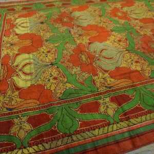 Red and orange rug with large green and gold botanical patterns on a weathered wood floor.