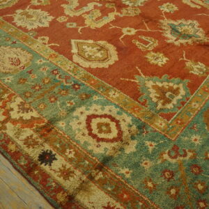 Textured rug with a rust field and wide teal floral border rests on rustic wood flooring.