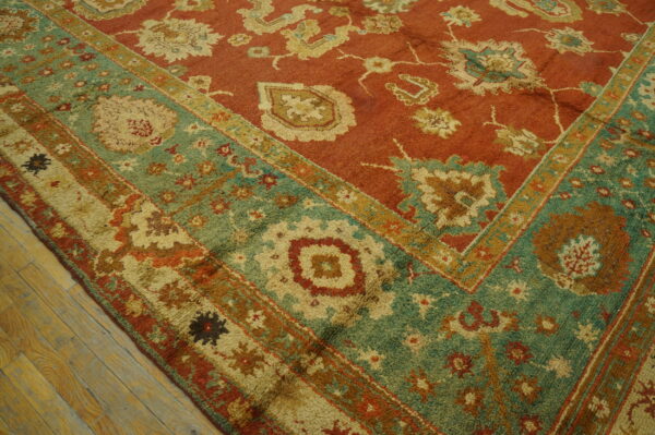 Textured rug with a rust field and wide teal floral border rests on rustic wood flooring.
