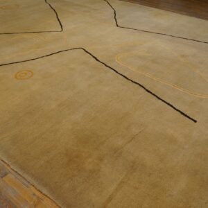 Golden low-pile rug with abstract dark brown and yellow designs lies on worn plank wood flooring.