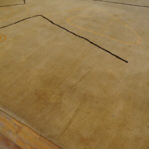 A golden beige rug with abstract dark brown and yellow designs lies on worn wood floors.