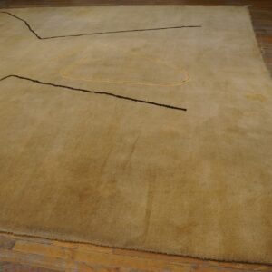 A textured tan rug with abstract black and gold linear designs rests on distressed hardwood.