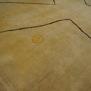 Muted yellow rug with dark geometric lines and flowing orange accents rests on distressed wood flooring.