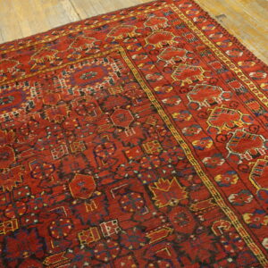 Low-pile red rug featuring dense geometric designs in blue and yellow on aged wood flooring.