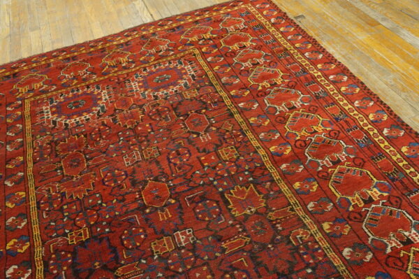Low-pile red rug featuring dense geometric designs in blue and yellow on aged wood flooring.
