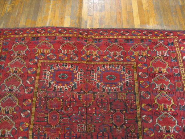 Close-up of a red tribal rug with detailed yellow and blue geometric patterns on a light brown wood floor.