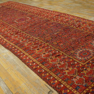 Geometric red runner rug with navy and yellow accents lying diagonally on light, distressed wood planks.