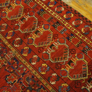 Red geometric rug with repeating yellow and blue medallions shown on bright yellow hardwood planks.