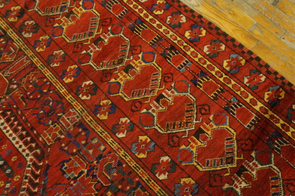Red geometric rug with repeating yellow and blue medallions shown on bright yellow hardwood planks.