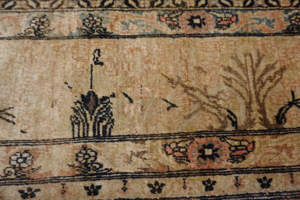 Muted tan rug detail featuring stylized scenic motifs and intricate borders with peach, blue, and black accents.