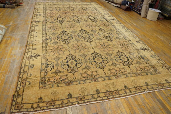 Low-pile rug in golden-tan with black and peach repeating motifs laid on hardwood.