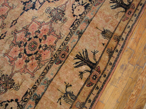 Low-pile rug featuring tan, black, and salmon traditional patterns bordered by distressed wood flooring.
