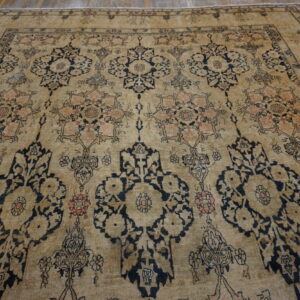 Low-pile beige rug with faded dark blue and coral traditional motifs covering a wood floor.
