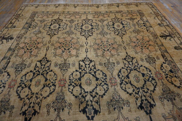 Low-pile beige rug with faded dark blue and coral traditional motifs covering a wood floor.