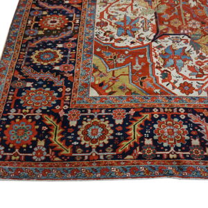 The corner of a traditional rug featuring complex floral borders in navy, red, teal, and cream.