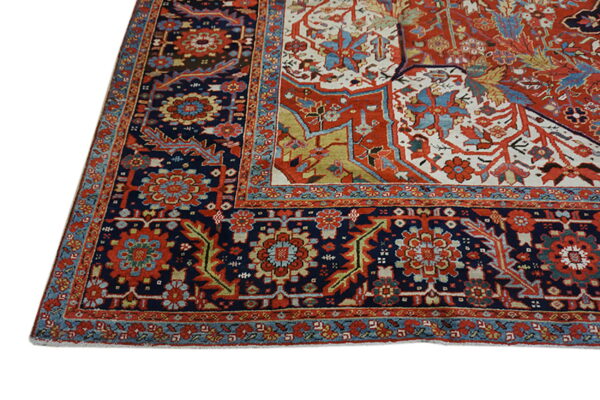 The corner of a traditional rug featuring complex floral borders in navy, red, teal, and cream.