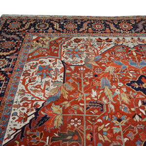 Detailed traditional rug featuring a rust red field with intricate blue, cream, and red floral motifs and borders.