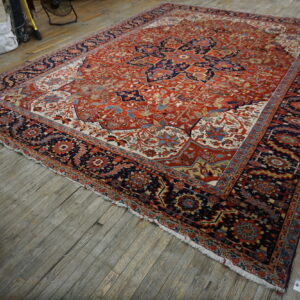 Traditional red and navy rug featuring a floral medallion, displayed on worn wooden flooring.