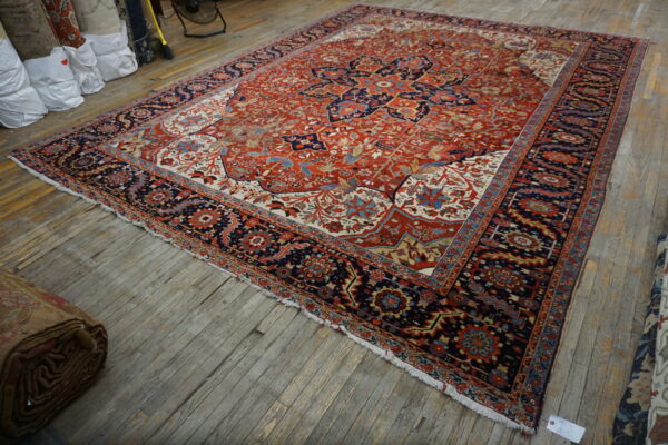 Traditional red and navy rug featuring a floral medallion, displayed on worn wooden flooring.