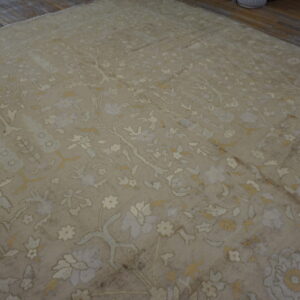 Distressed beige rug with a dense cream and soft gold floral pattern resting on dark hardwood.