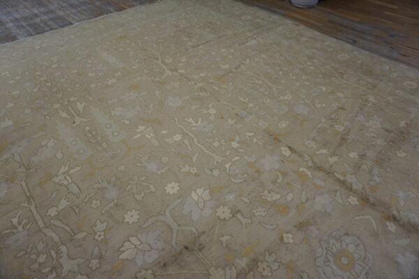 Distressed beige rug with a dense cream and soft gold floral pattern resting on dark hardwood.