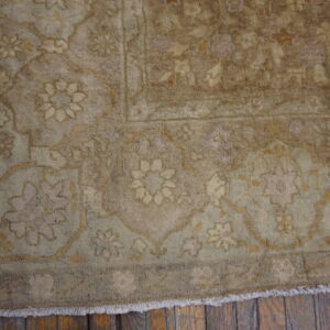 Muted beige and tan traditional rug with a detailed floral pattern and fringe on rustic wood flooring.