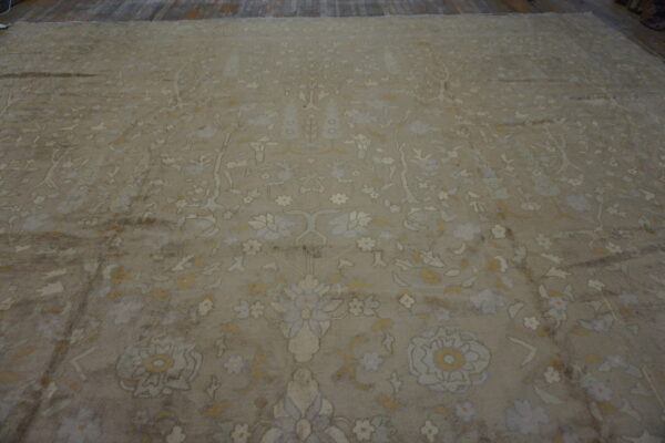 Beige distressed rug with a dense botanical pattern in cream, pale yellow, and light blue on wood floor.