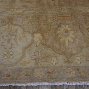 Muted, high-pile rug detail showing floral patterns in brown, beige, and sage over distressed wood flooring.